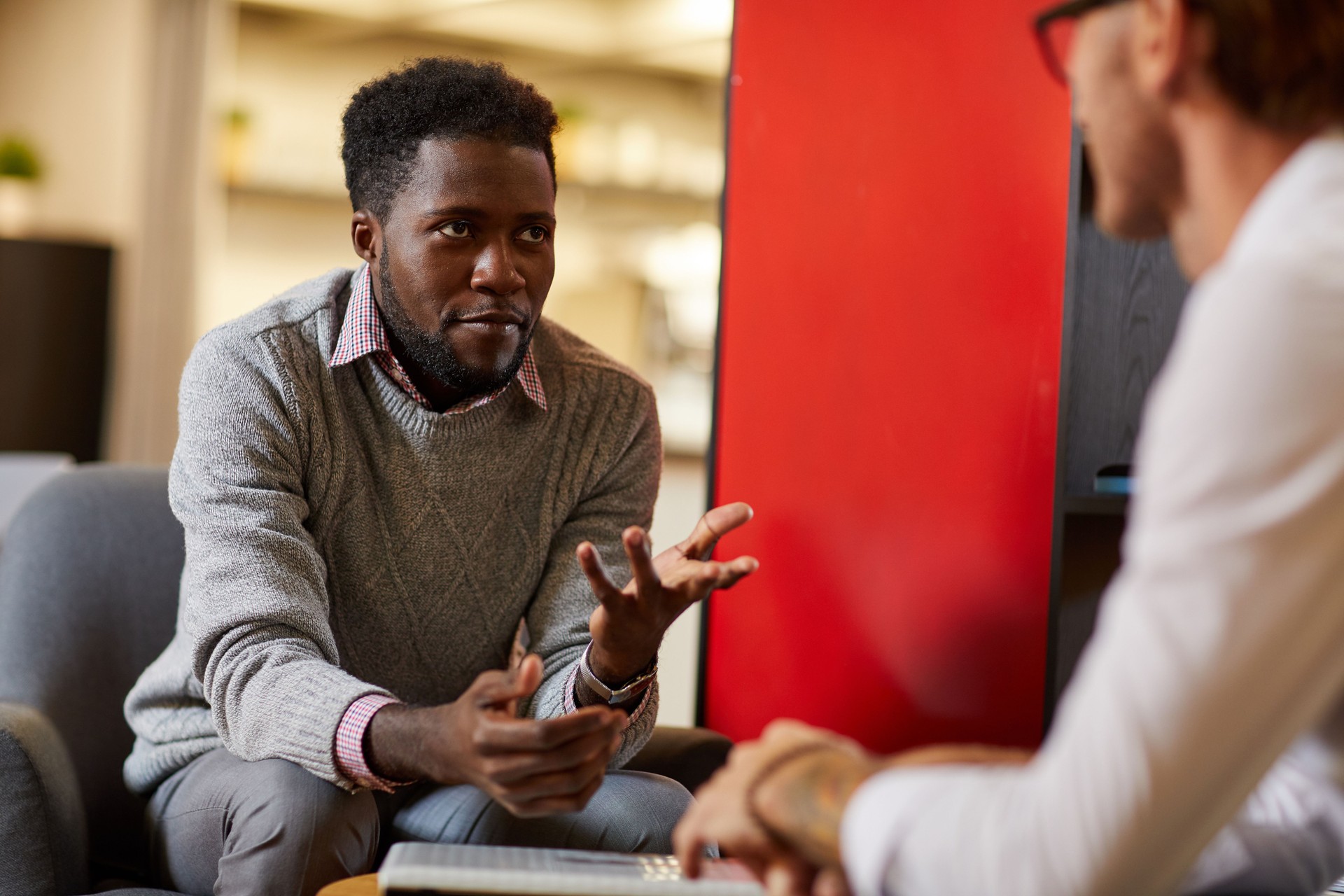 Content confident bearded Black man gesturing hands while explaining idea to colleague in modern cafe